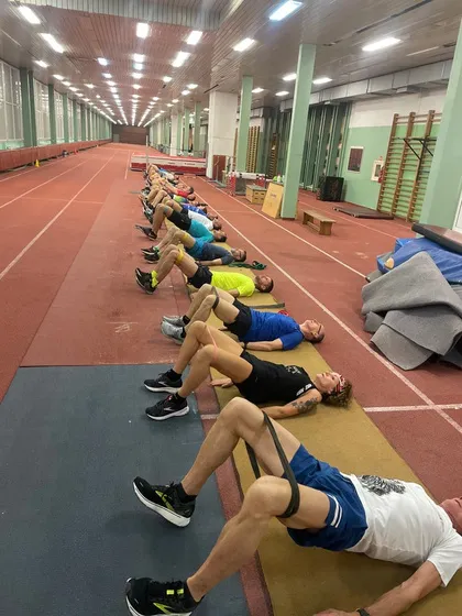 Grupa uczestników wykonuje ćwiczenia na macie w hali sportowej